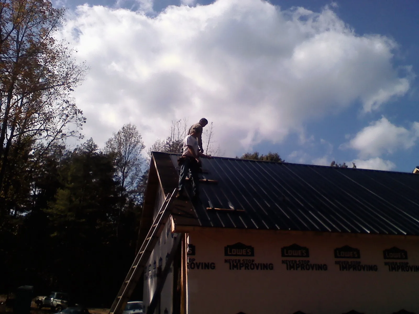 Roofer fastening dark metal panels high against a cloudy sky, from a Roof Inspection job in Hinsdale